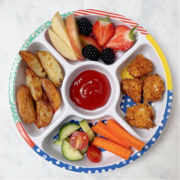 airfryer chicken nuggets served on a children's divided plate with potato wedges, and chopped fruit and veggies