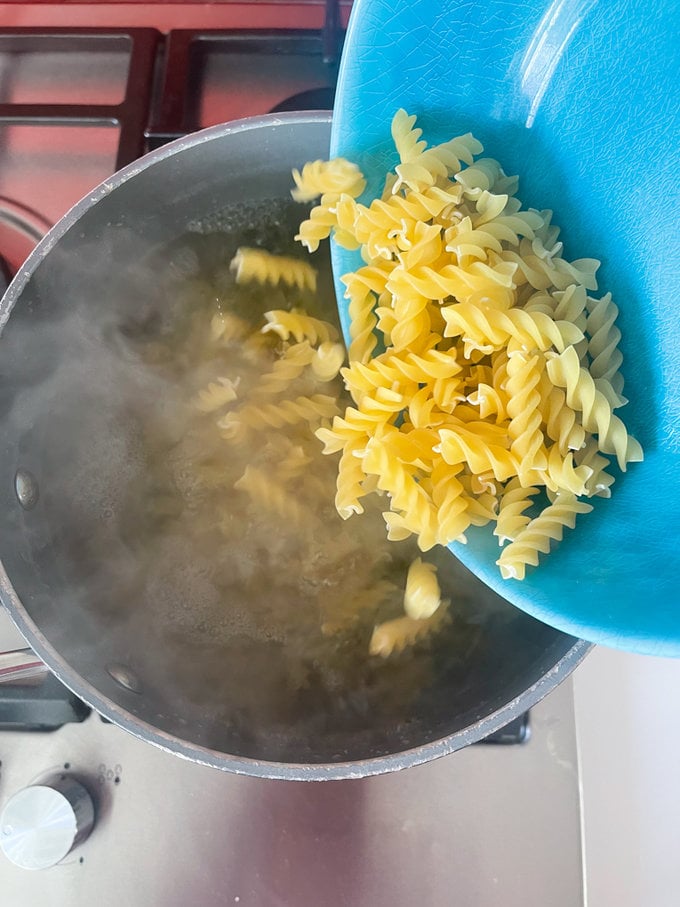 pasta being poured into boiling water to cook