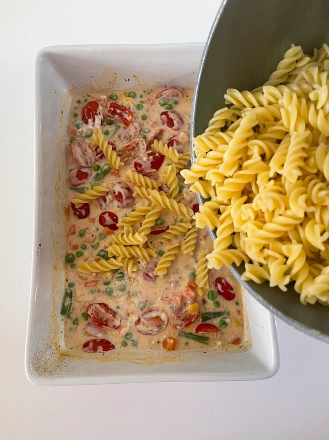 the cooked pasta being added to the ingredients in the oven proof dish