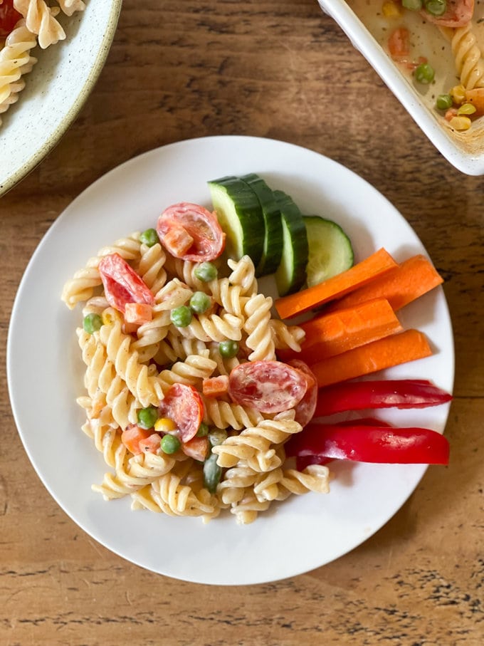 a small serving for kids of the baked cream cheese pasta on a white plate with some chopped raw vegetables on the side