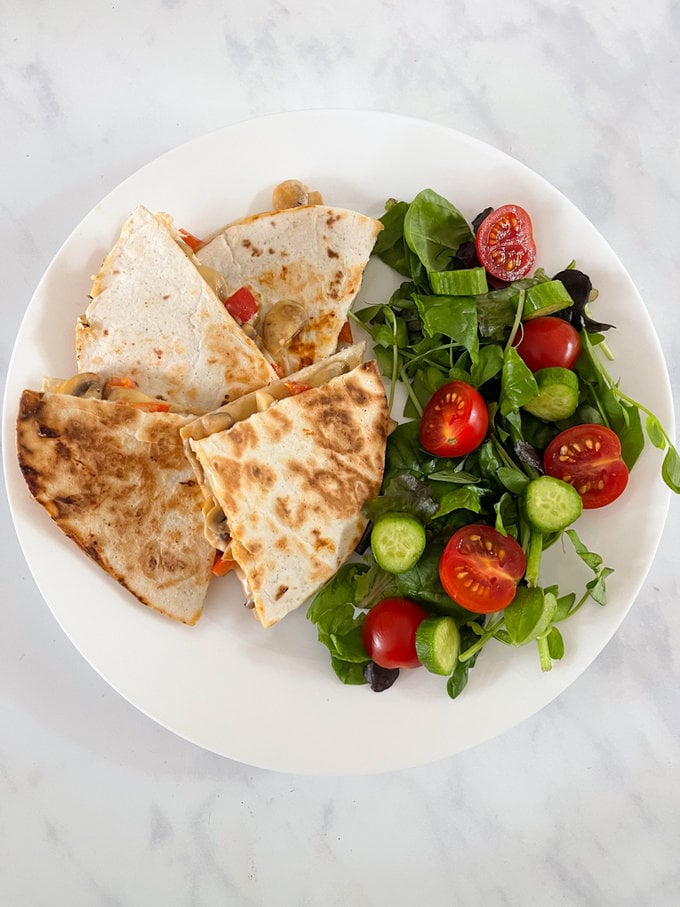 Cheesy veggie quesadillas served on a white plate alongside a small salad.