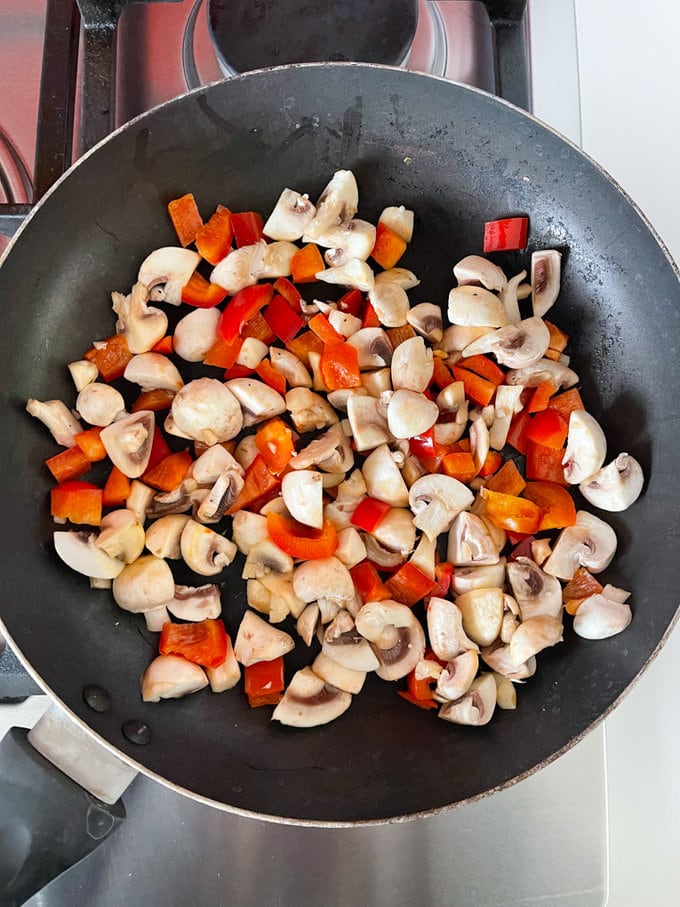 Mushrooms and peppers cooking in a frying pan.