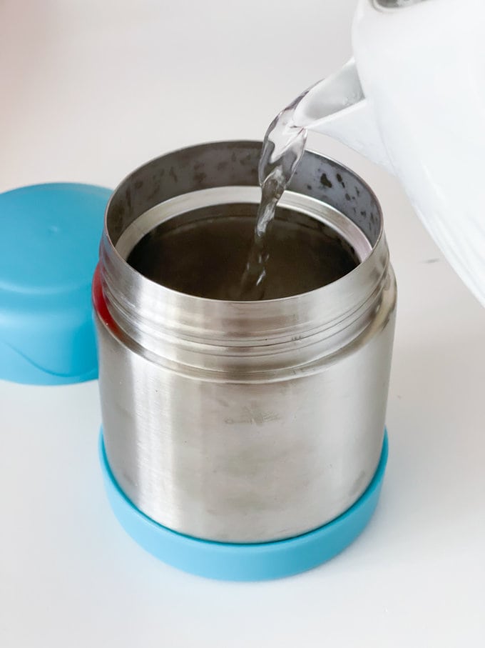 Food flask being prepared with boiling water from a kettle.