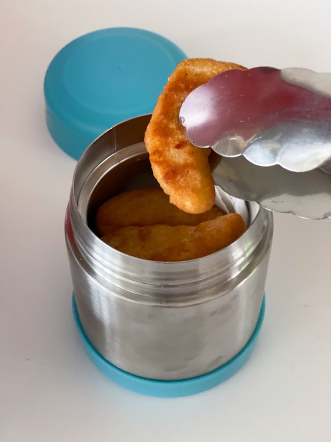 Cooked nuggets being placed into the food flask with tongs.