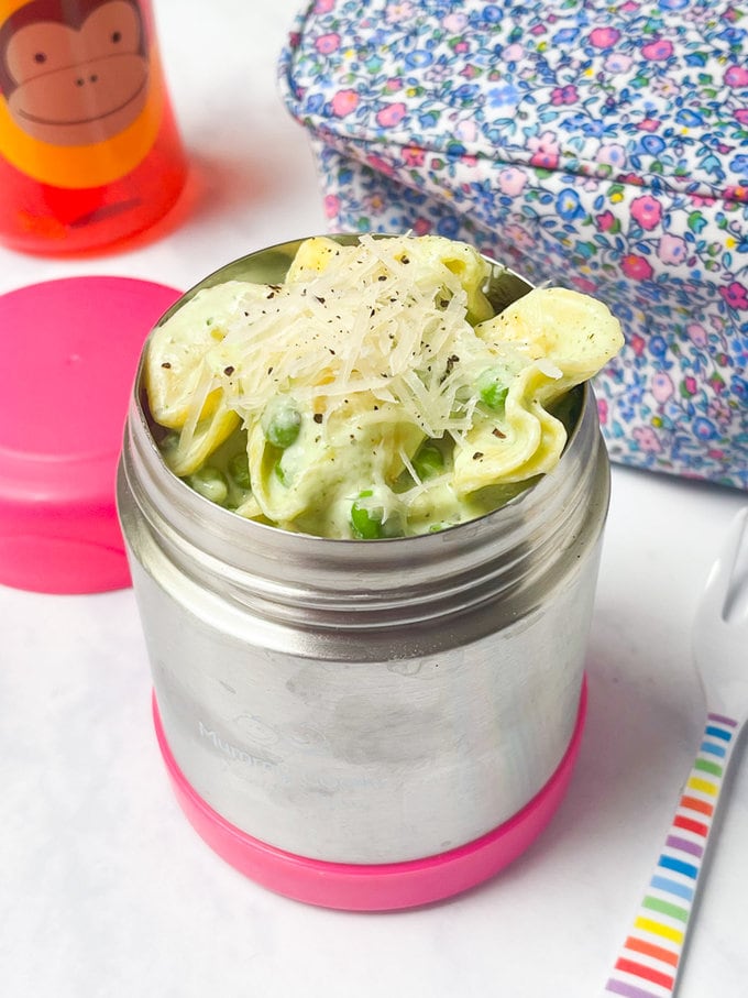 Creamy basil tortellini served in a food flask with grated cheese on top.