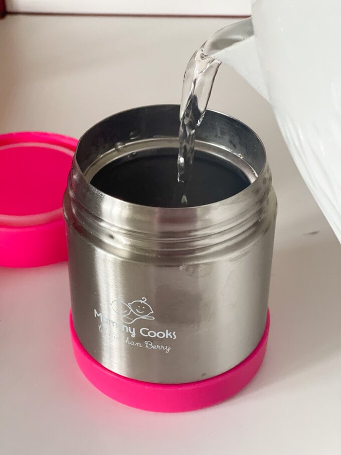 Hot food flask being prepared with boiling water from a kettle.