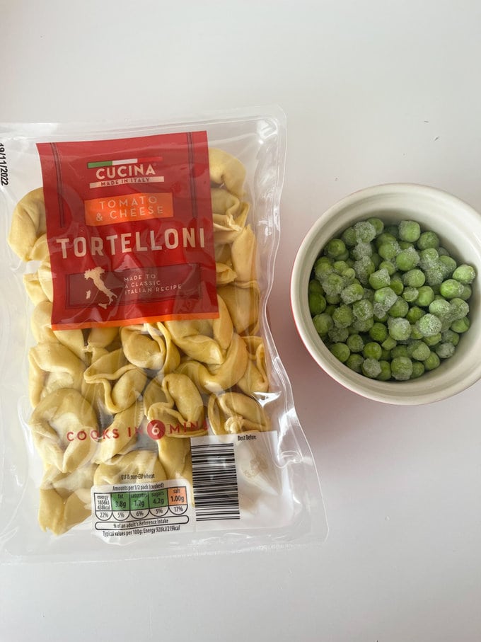 Tortellini in its original packaging, with a small pot of frozen peas beside.