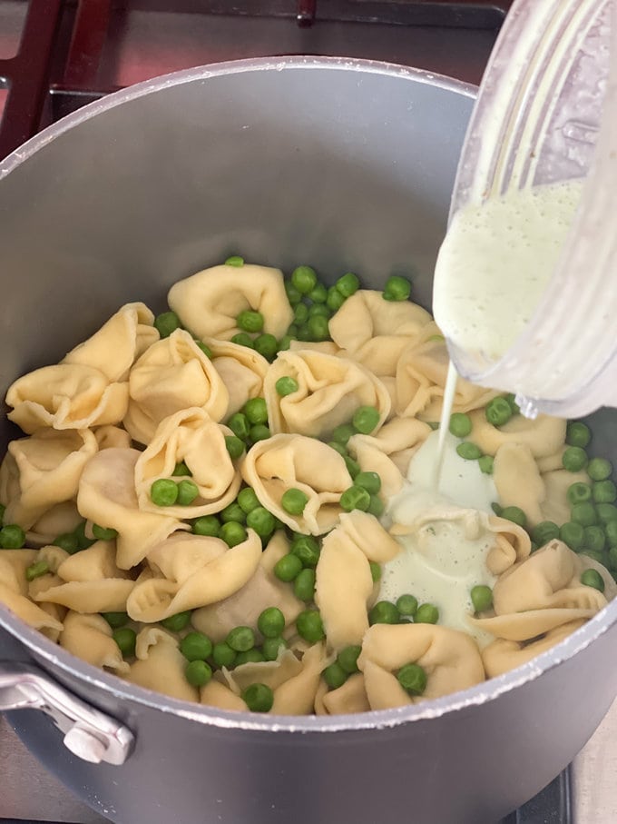 sauce being poured over the cooked tortellini and peas.
