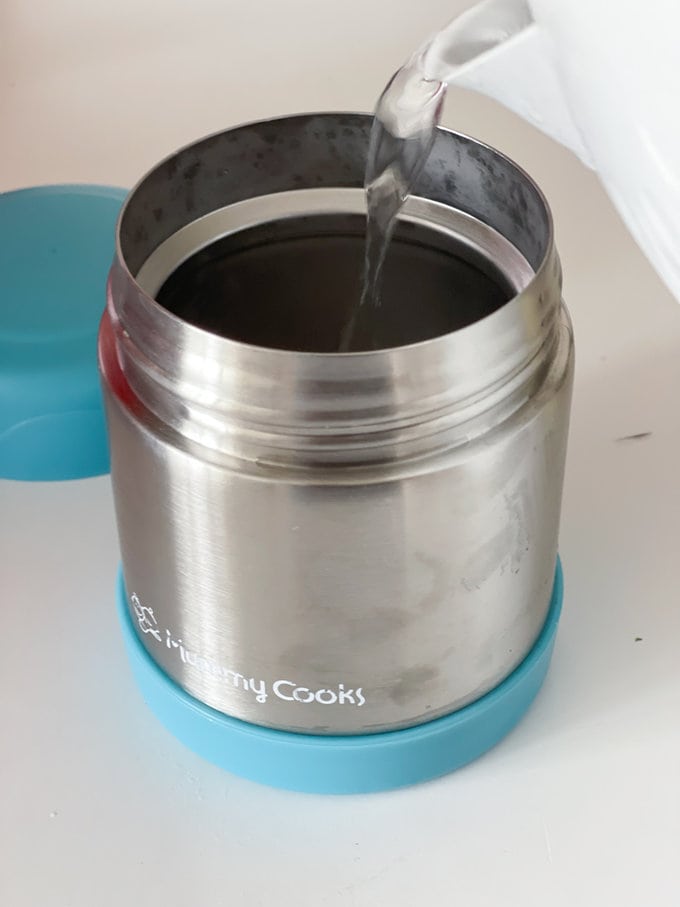 Boiling hot water from a kettle being poured into food flask in preparation.