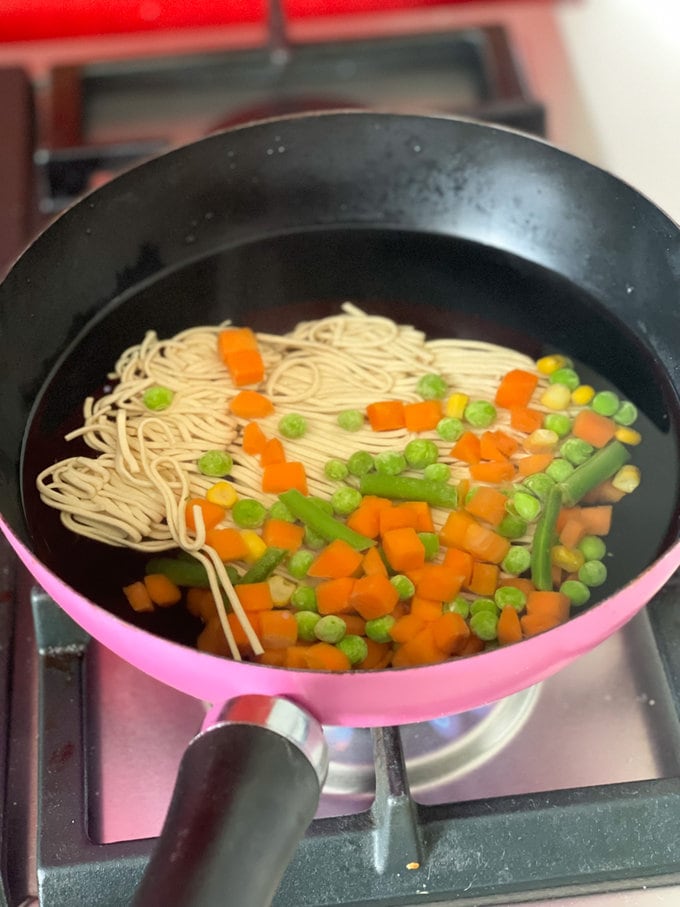 Dried noodles & frozen vegetables in a pan ready to be cooked.