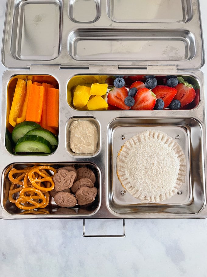 Crustless sandwich served in a metal style lunchbox, along with other fruit, vegetables and other treats.