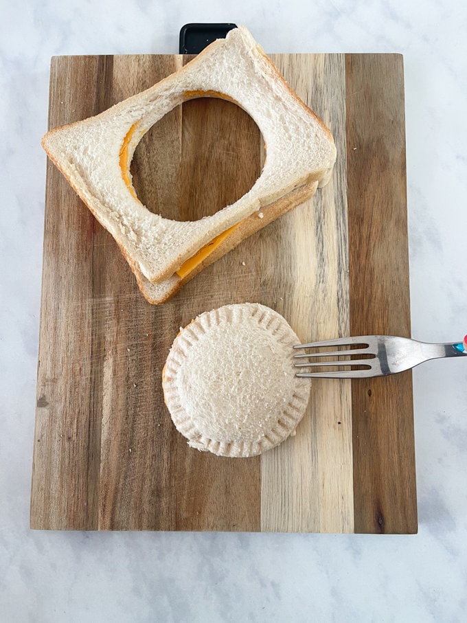 Sandwich cut into a round shape using the pastry cutter, and a fork is being used to crimp/seal the sides.