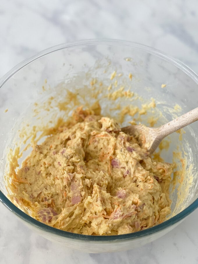 ingredients all being combined in a glass mixing bowl using a wooden spoon. 