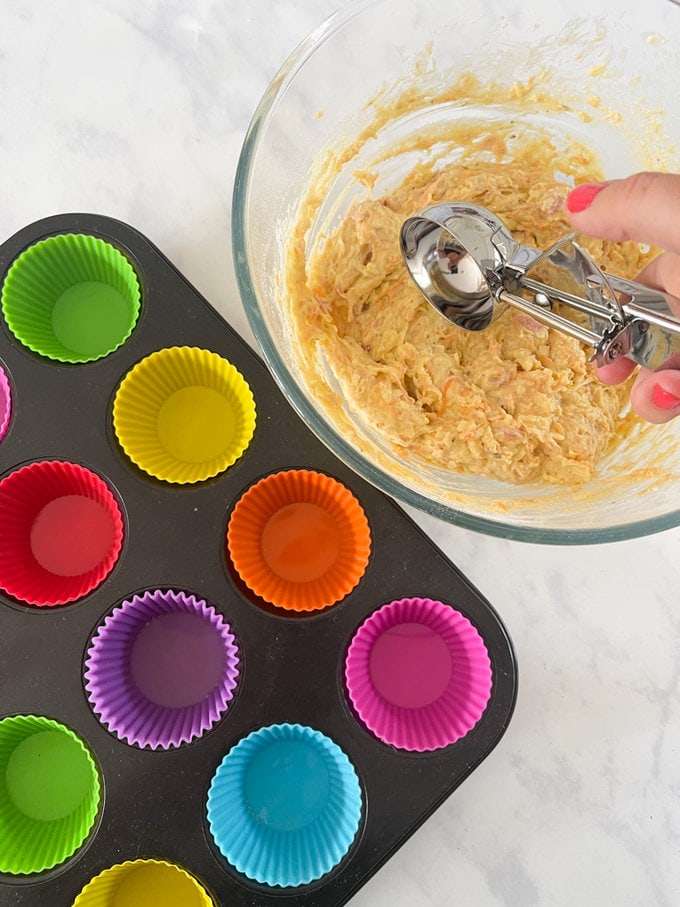 Muffin mix being transfer from mixing bowl into cupcake cases using an ice cream scoop to ensure equal amounts.