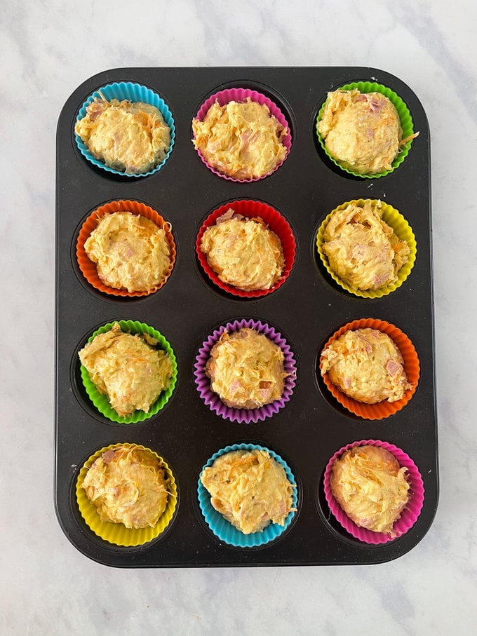 uncooked Muffins presented in cupcake cases on a baking tray ready for the oven.