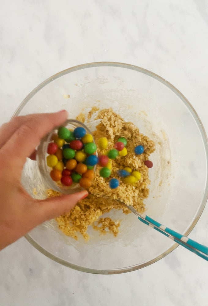 M&M being added to the cookie mixture.