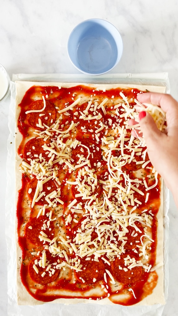 Cheese being sprinkled over the puff pastry once the pasatta has been added.