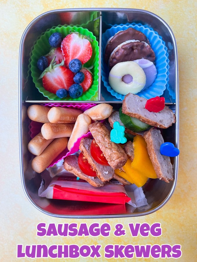 three compartment stainless steel lunchbox with sausage and veg mini skewers, fruit, veg, mini breadsticks, cheese portion, mini party rings and mini rice cakes.