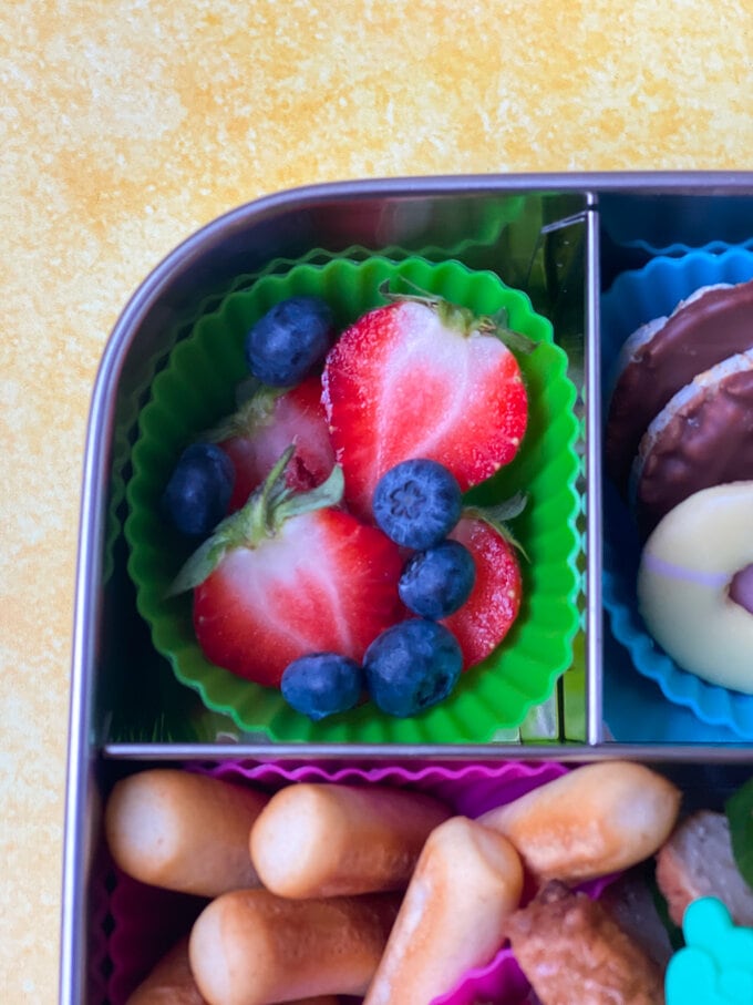 Sliced strawberries and blue berries severed in a green cupcake case.