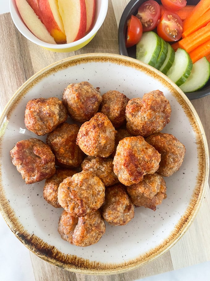 Air fryer cheesy sausage bites presented in a small bowl alongside chopped cucumber, Carrots & cherry tomatoes. 