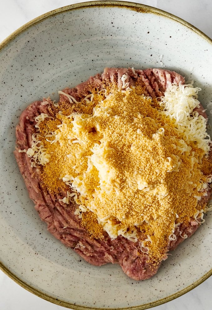 Cheese and breadcrumbs being added to sausage meat in bowl.