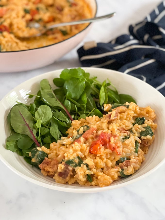 Risotto presented in a medium sized white bowl, with Spinach on to one side.