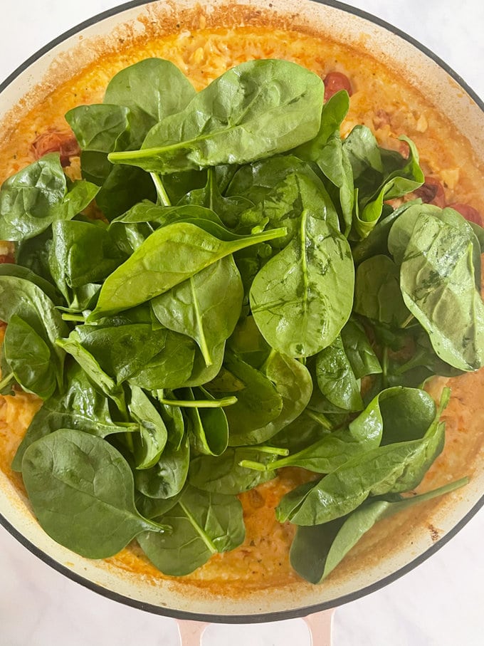 After 30 minutes, remove from the oven and stir in some fresh spinach. The heat from the risotto will wilt the spinach as you mix it in, all presented in white oven proof dish. with Spinach on top.