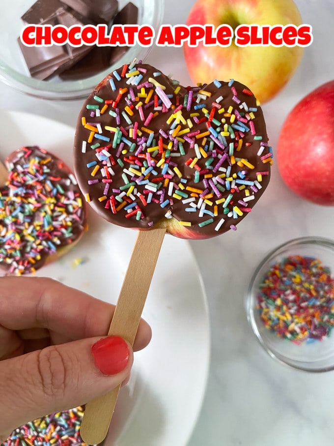 chocolate apple slices on a stick covered in chocolate and decorated with multicoloured sprinkles.