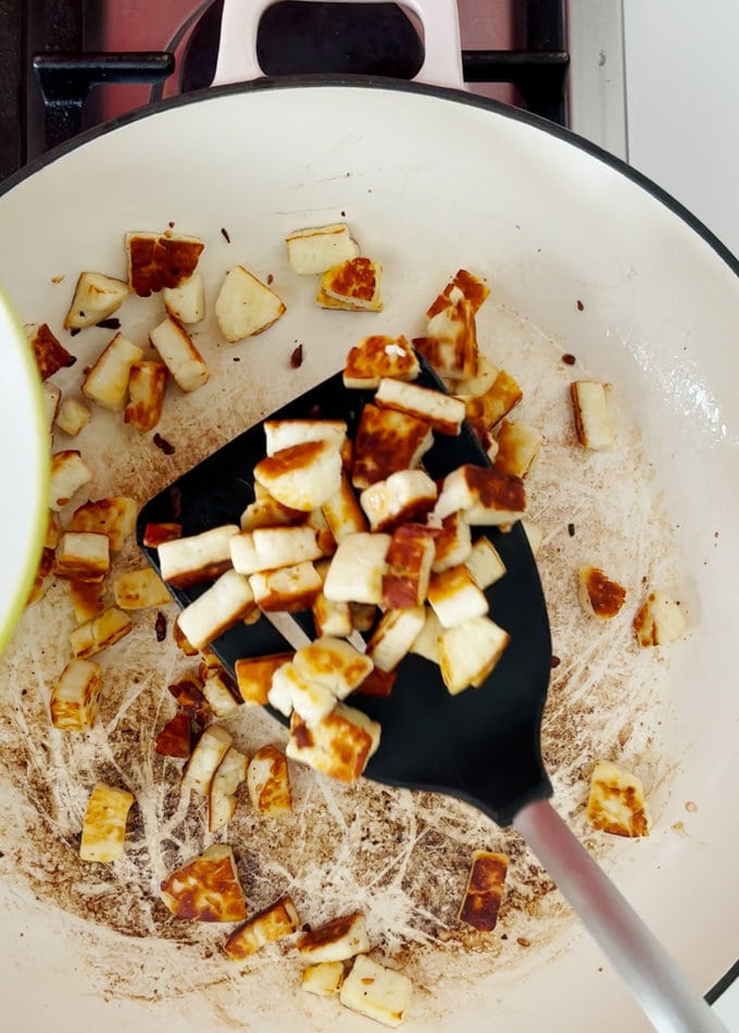 Crispy and browned Halloumi being removed from pan, and set aside on a plate on a plate.