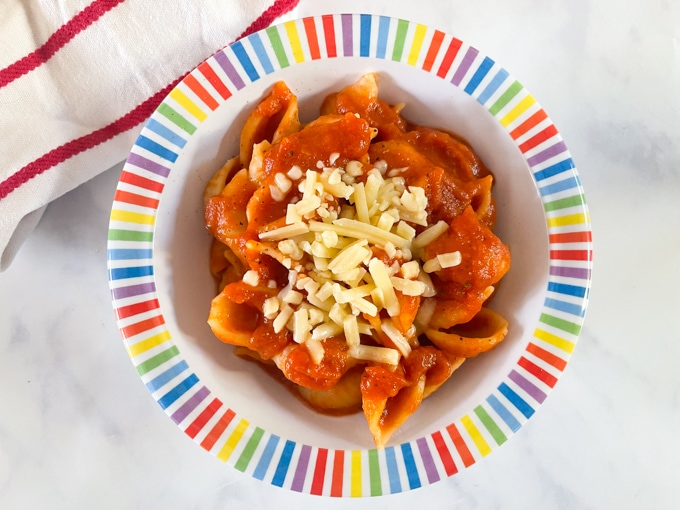 Slow Cooker Hidden Veggie Pasta Sauce served in a colourful children's bowl with pasta and grated cheese.