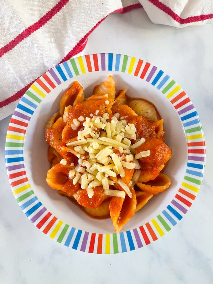 Slow cooker hidden vegetable pasta sauce served over pasta. in a colorful bowl garnished with grated cheese.