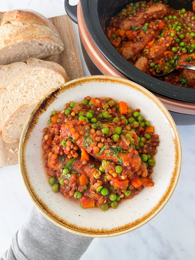 Slow cooker sausage and lentil casserole served on a plate with a side of crusty bread.