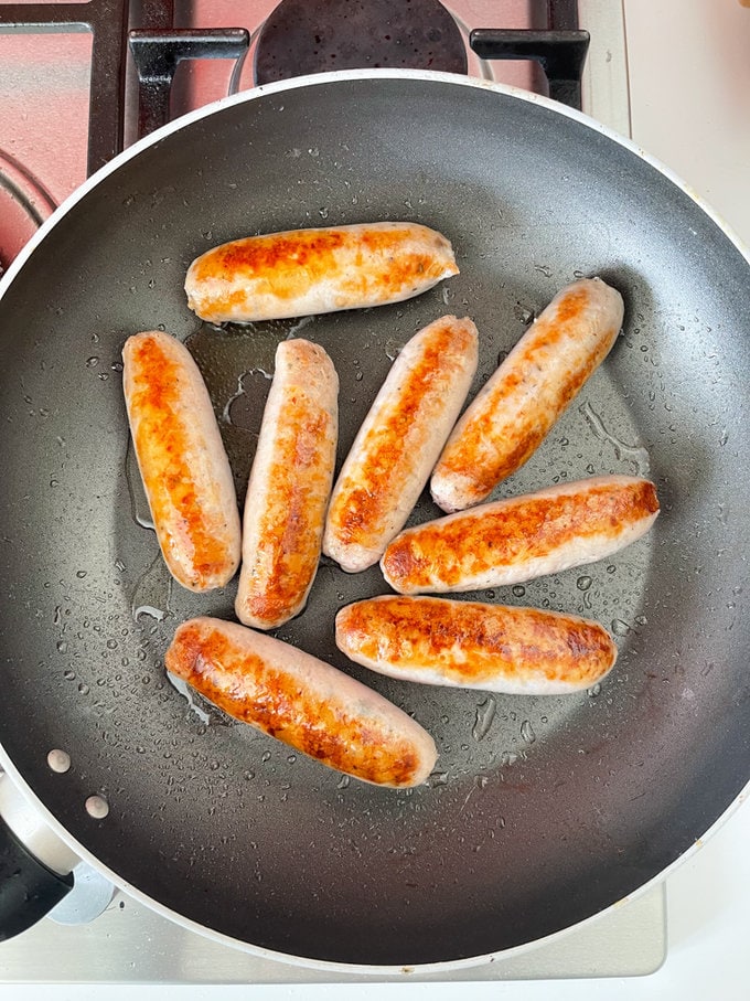 Sausages being browned off in a frying pan.