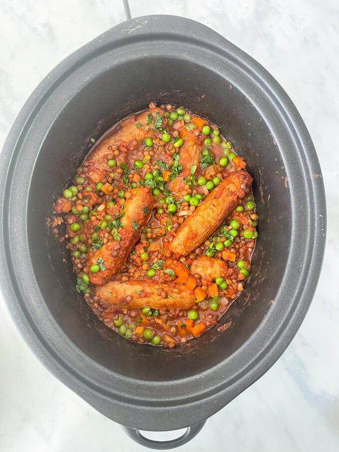 Cooked Sausage and lentil casserole in slow cooker with lid off garnished with chopped fresh parsley.