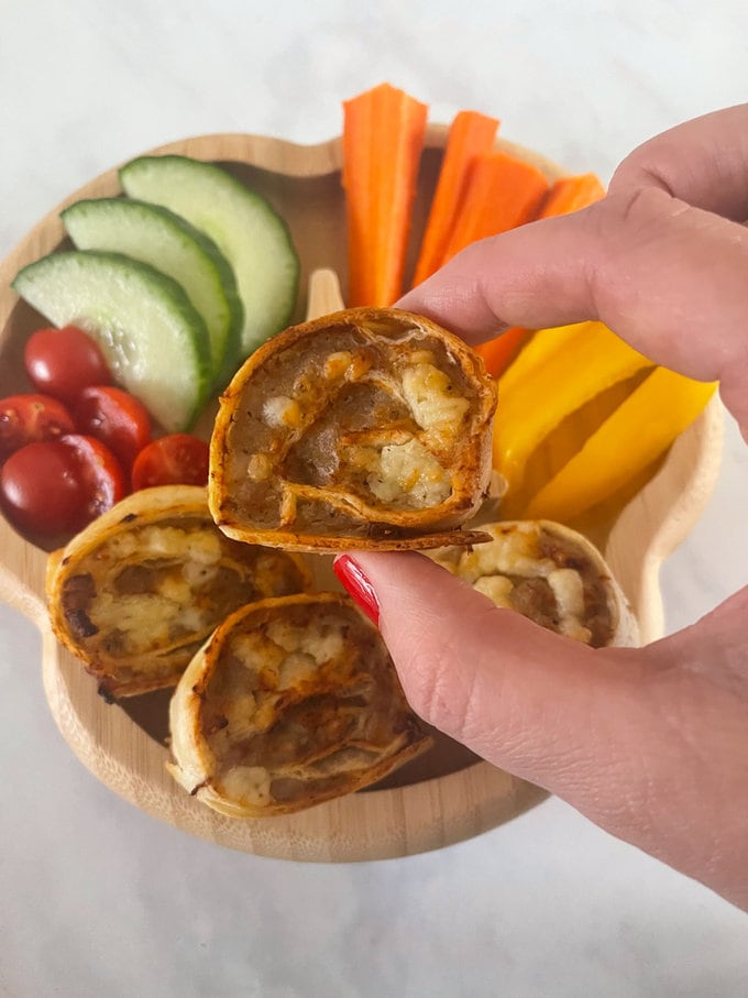 Cheesey sausage pinwheels presented on a child's wooden plate along with fresh tomato, cucumber and peppers.