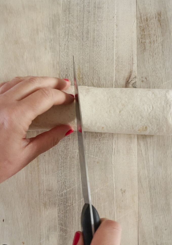 Rolled tortilla being cut into equal pieces.