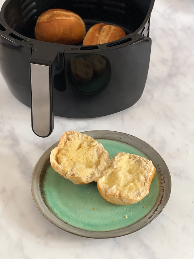 Cooked part baked airfryer roll served on a plate with lots of butter spread over.