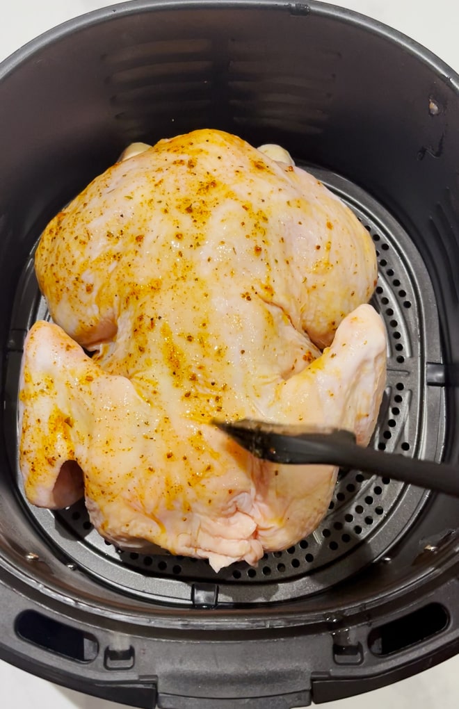 Raw chicken sitting in the airfryer being prepared for cooking.