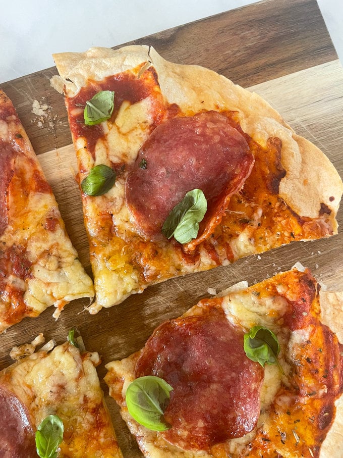 Crispy air fryer pizza cut into four pieces and served on a wooden chopping board and garnished with basil. 