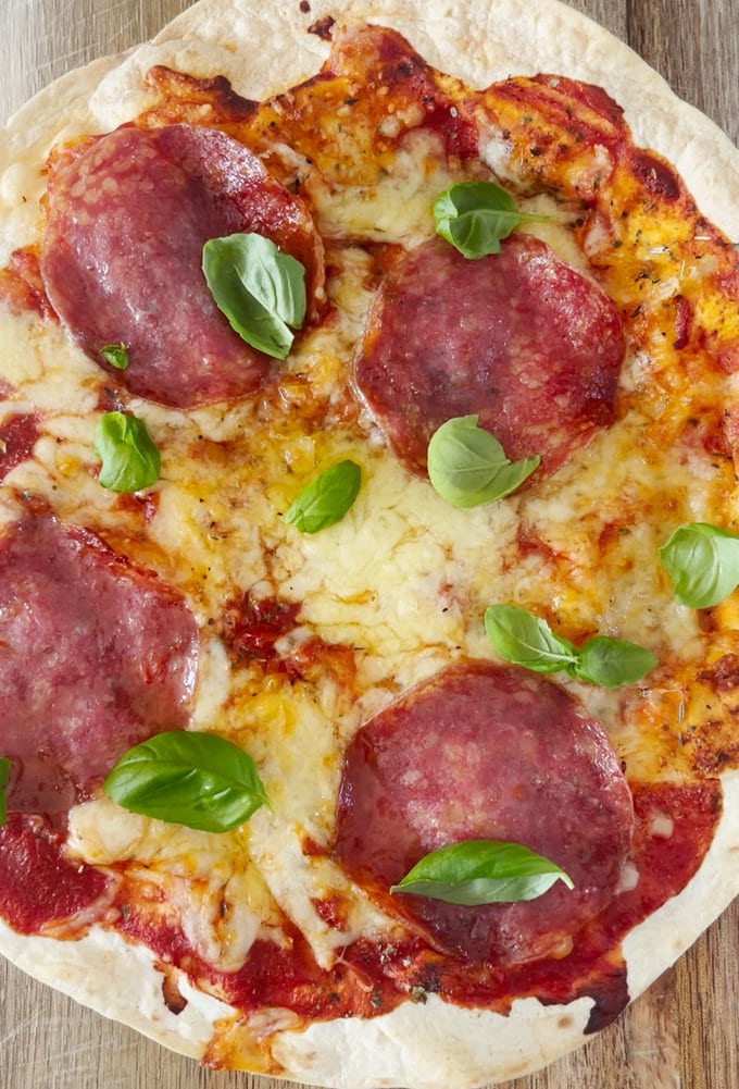 Airfryer Tortilla Pizza garnished with fresh basil leaves and served on a wooden chopping board.