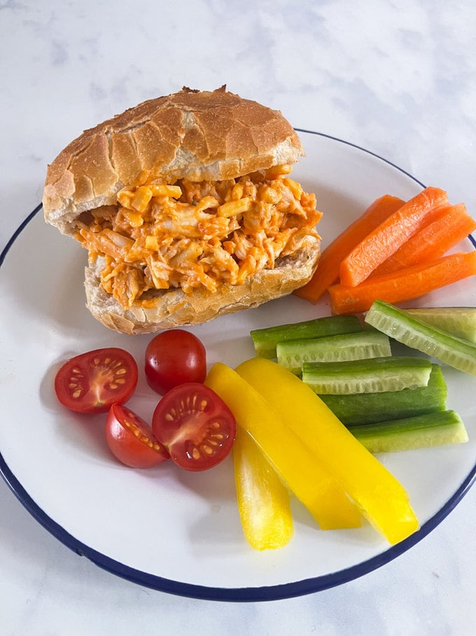 Airfryer roll filled with cheesy buffalo chicken. garnished with fresh, raw carrots, cucumber, cherry tomatoes and yellow peppers.