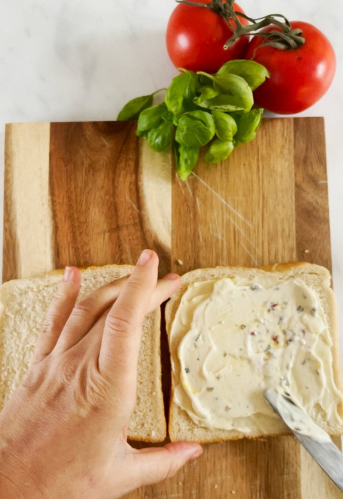 Cream cheese being spread over two slices of bread.