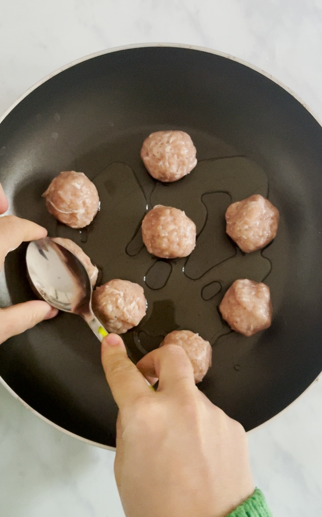 Chicken meatballs being fried in a little oil in a black pan.