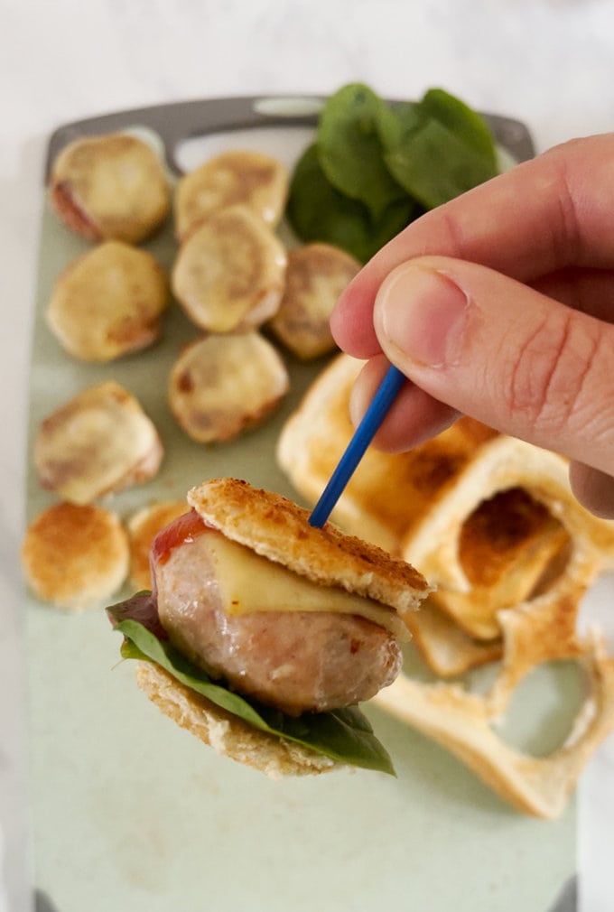 Close up of complete mini chicken burger, being held together with a blue pick stick.