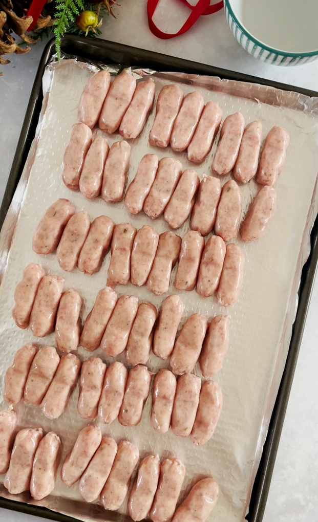 raw cocktail sausages laid out on a baking tray that has been lined with foil
