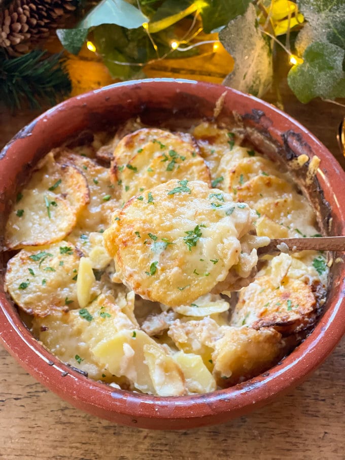 Golden brown airfryer dauphinoise potatoes presented in a brown heatproof dish and garnished with fresh parsley. 