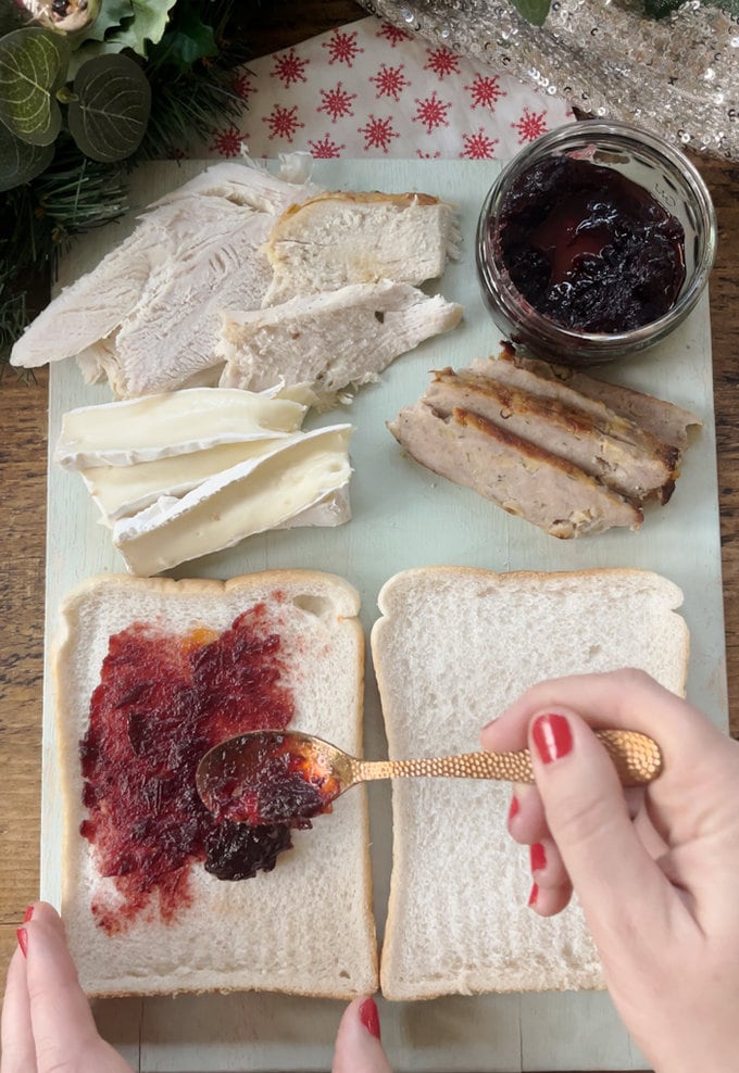 Turkey, Brie, stuffing and Cranberry sauce being added to bread on chopping board.