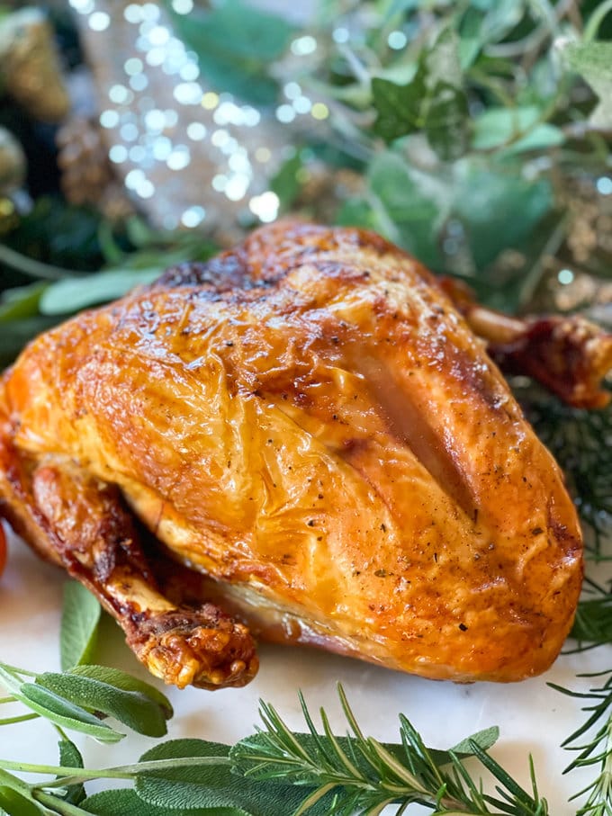 Golden air fryer turkey crown sitting on a bed of green herbs.