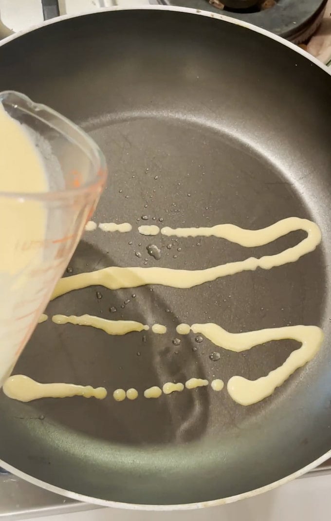 Pancake mix being poured into a frying pan.