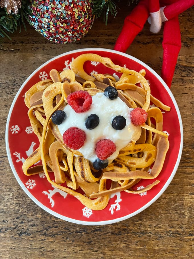 Elf spaghetti presented on a red plate with white reindeer decoration.  Spaghetti garnished with Greek yogurt and berries. 